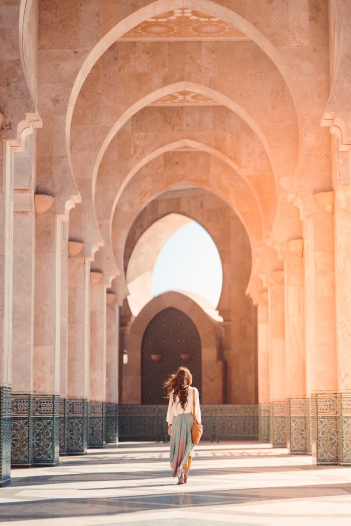 A woman walks through the stunning arches of Hassan II Mosque, Casablanca, highlighting Islamic architecture.